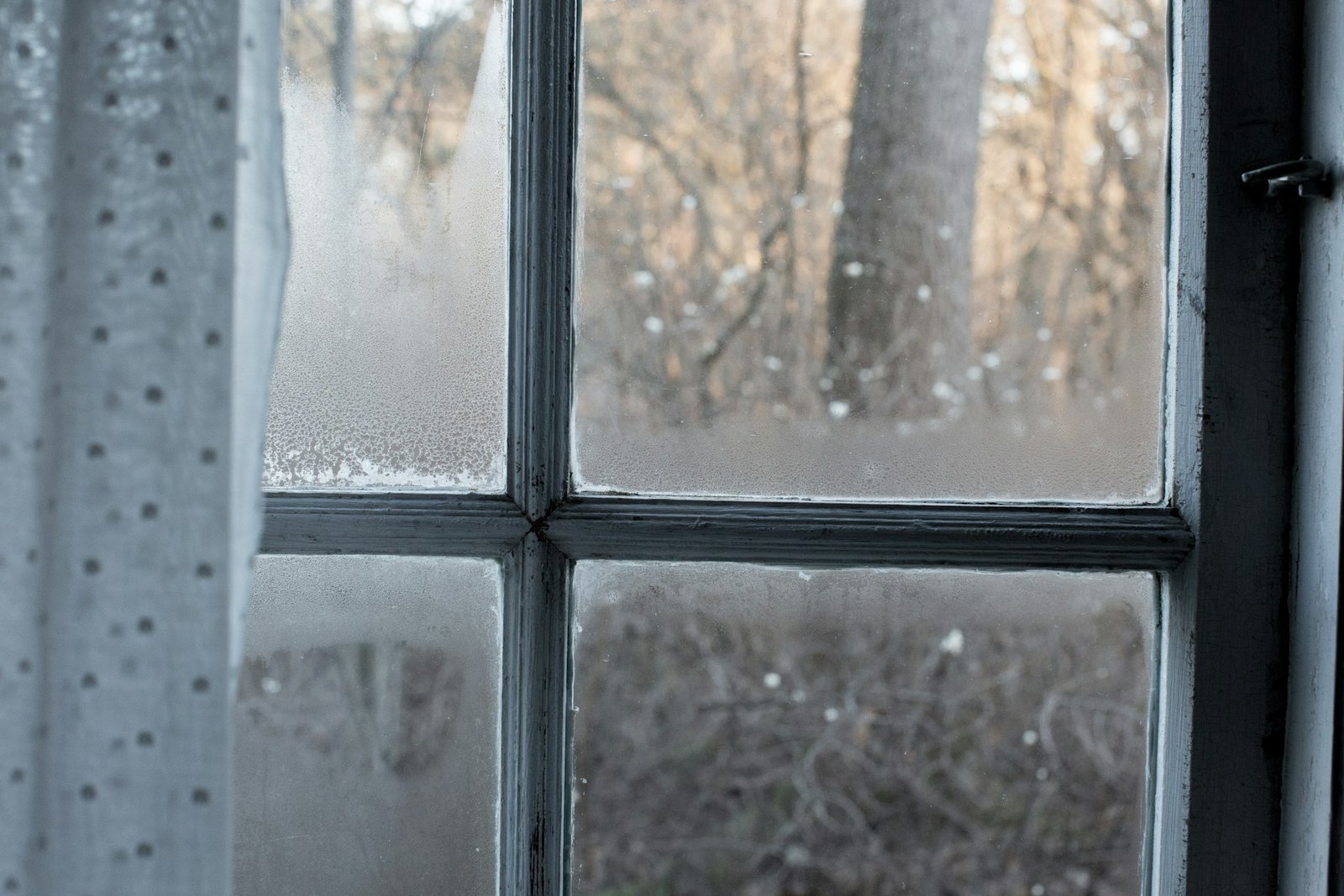 Geschlossenes Fenster mit Frost am Glas und Hand am Fenstergriff